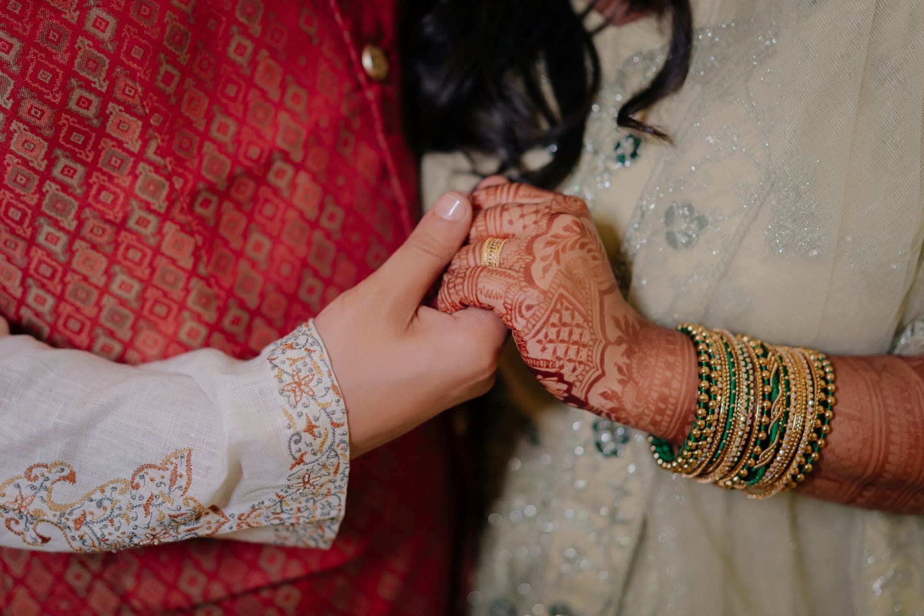 Two hands held together at a wedding, bangles and mehndi catching the light